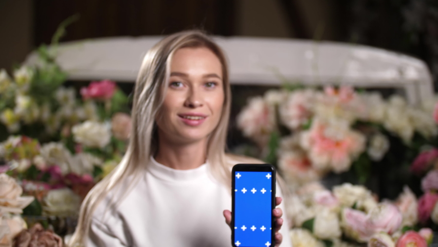 Lady slides swipes chroma key blue screen. Female person holds smart phone device in hands with chromakey. Fit woman on flower background portrait with smiling face looks at camera with blue screens