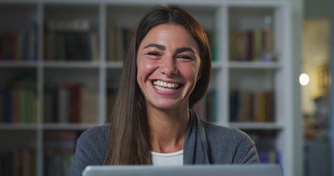 Cinematic shot of young business woman is smiling satisfied with her work while doing smart working with laptop from home in living room during lockdown with soft atmospheric light.