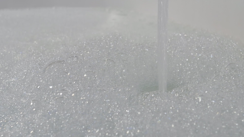 Bathtub with soap suds. Preparing a bath, hot water flows from the tap. Foam with bubbles popping in warm water.