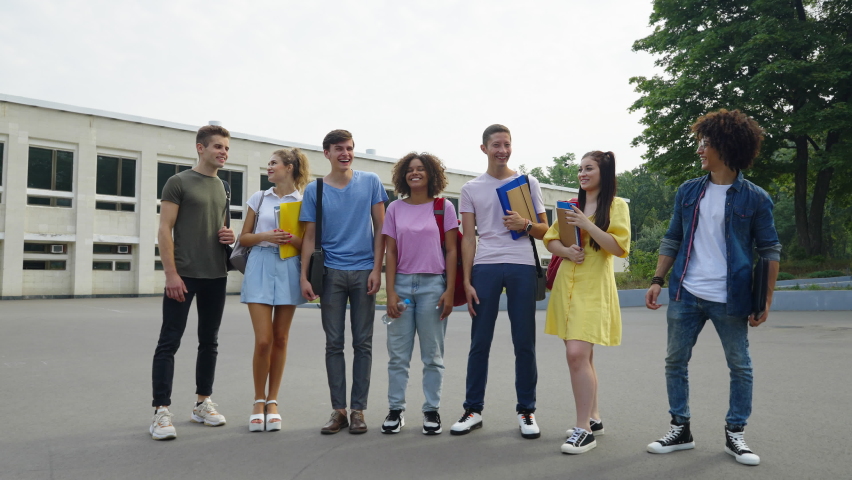 Cheerful students standing in front of college building and showing thumbs up. Multiethnic friends giving approval. Concept of education