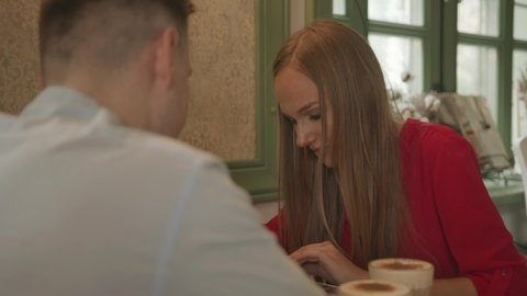 A man and a beautiful young girl are sitting at a table in a vintage cafe are laughing and looking at the menu
