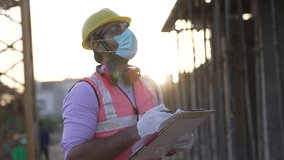 Young Indian happy man engineer matching details with blue prints and site plans on site.Asian male wearing protective face mask or helmet making plans for their project on construction site outdoor. - Powered by Shutterstock - Get 15% off with code: PIKWIZARD15