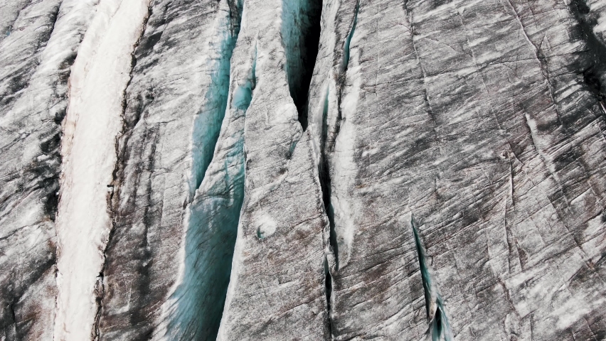 Large high grey cliffs with blue shadow rifts and big deep cracks covered with snow and black mineral products aerial view