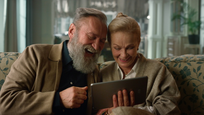 Excited senior couple looking tablet computer in luxury house. Portrait emotional old people using digital device on sofa in living room. Close up happy family having fun spending time together home Royalty-Free Stock Footage #1079534174