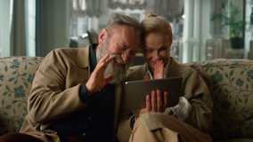 Happy senior old couple talking relaxing using digital tablet computer on sofa. Cheerful mature elderly people having fun enjoy spending time with gadget at home. Happy grandparents video call tablet - Powered by Shutterstock - Get 15% off with code: PIKWIZARD15