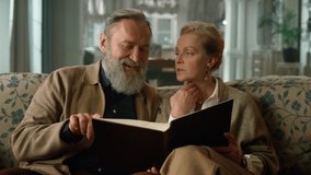 Elegant senior couple looking family album in classic living room. Attractive old man and woman spending time together in luxury apartment. Pleasant elderly people talking about photo album indoors. - Powered by Shutterstock - Get 15% off with code: PIKWIZARD15