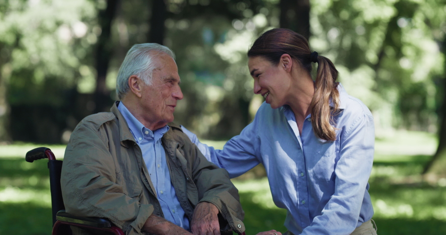 Cinematic shot of happy granddaughter is giving an affective hug to grandfather with disability who uses wheelchair as sign of love and respect in green park.  Royalty-Free Stock Footage #1079534564