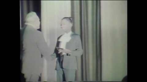 1970s: FBI agent receives diploma from academy in ceremony. Two FBI agents get in car, drive around. FBI building. Agents, employees at work in offices.
