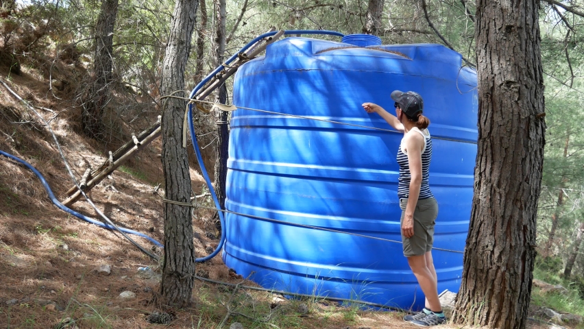 The girl knocks on a large container to determine the water level.