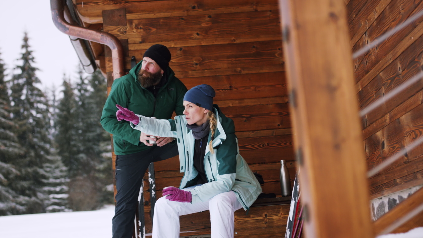Mature couple resting by wooden hut outdoors in winter nature, cross country skiing.