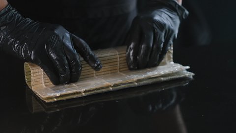 Professional sushi preparation in a Japanese restaurant. Sushi maker with black gloves prepares seafood sushi. Traditional Japanese cuisine.