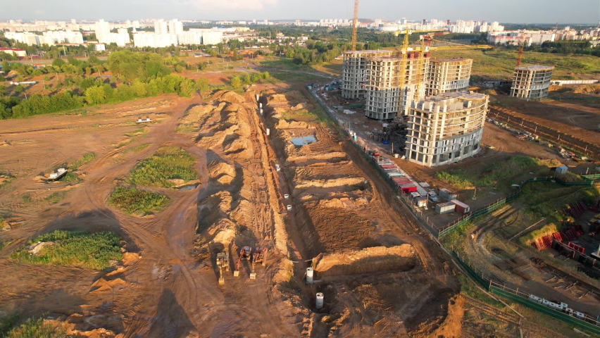 Construction site fron drone view. Laying of storm sewer pipes and sewerage wells and concrete well ring. Drainage concrete pipe. Tower crane during construction of a residential building. 
