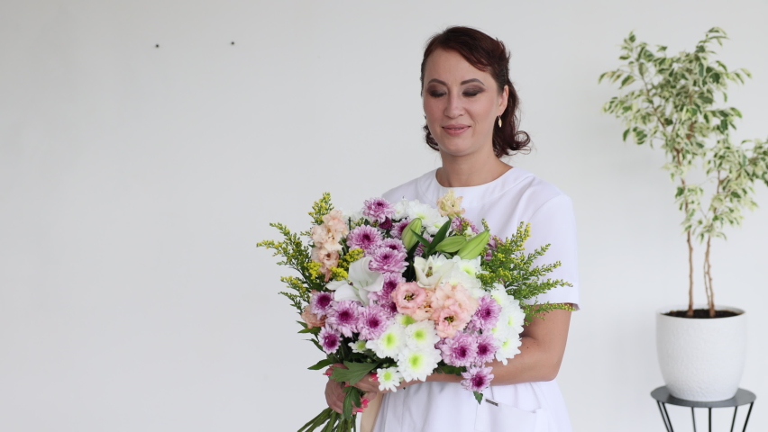 Caucasian woman in a white coat with a large bouquet of fresh flowers. day of the medical worker. gratitude to the doctors. Cosmetology and medical services office.