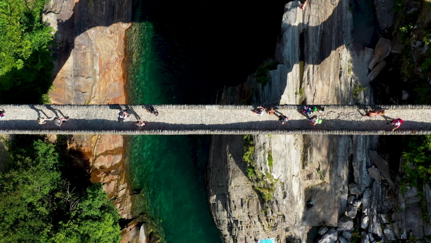 Downward angle drone shot of Ponte dei Salti the double-arched medieval stone pedestrian bridge over the clear water of the Verzasca River. In Lavertezzo in Switzerland.