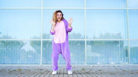 Funny cheerful happy young woman dancing outdoors on blue wall. Crazy female hipster girl in a dress unicorn costume mask dance. Concept fun people, happiness, joy Modern lifestyle in city street