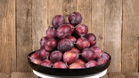 Plate of plums on wooden background. Loop motion. Side view. Rotation 360. 4K UHD video footage 3840X2160.