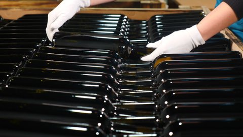 Wine production factory. Female worker in white gloves arranging wine bottles in container or wooden box. composing glass bottles of wine into shipping container in store. Preparation for shipment to