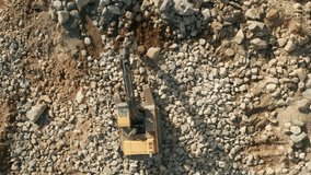 Tractor with large jackhammer crashing stones, preparing ground for construction site. Aerial top down video