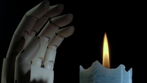 Closeup shot of a burning candle rotating and a mannequin hand. Religion concept. Creepy candlelight. Dark blue candle. Studio shot. Black background.