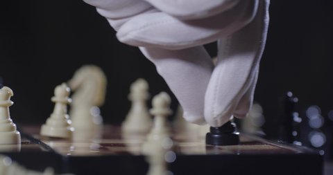 Chessboard extreme close-up. Two unrecognizable persons in white cloth gloves play chess, move pieces and make moves. The black chess pawn makes a move and becomes a queen