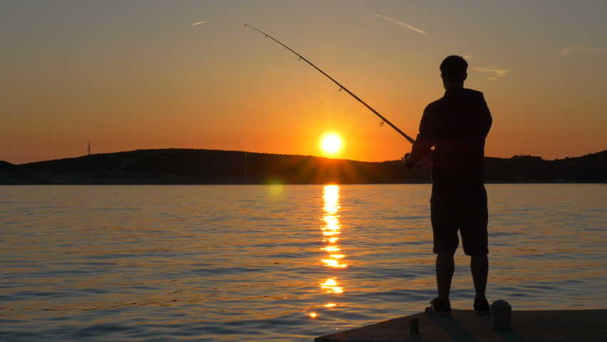 Fisherman standing on pier and winding up the fishing line