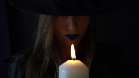 witch with black lips blows out the candle. Halloween party celebration. Witchcraft on a dark night. Woman doing occult event. Mysterious video. Dark intimidating action. Frightening darkness