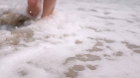 a girl walks along a sandy beach washed by a sea wave. Feet close-up. Footprints. Vacation, travel around the world. Beautiful female legs. Tour. Rest by the sea, the ocean