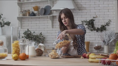 Woman pouring corn flakes in glass bowl. Healthy woman poring cereal muesli for breakfast. Health girl preparing cornflakes breakfast