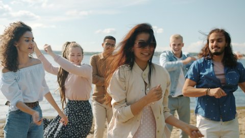 Slow motion portrait of girls and guys dancing jumping having fun on beach on summer day. Leisure time activities and positive emotions concept.