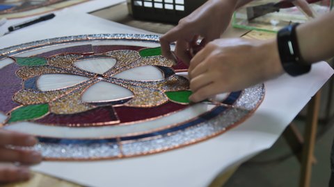 Two artists assemble a composition from stained glass windows. Assembling parts from a stained-glass window. Hands of two women. Craft, handmade. Tiffany stained glass. Details of the picture. 