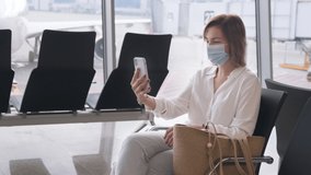 Young woman using mobile phone and calling with video to her business partner or friends in terminal of international airport. Face mask is on her face for safety and prevention coronavirus infection.