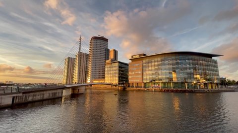 Salford Quays, England. Sept 22, 2021. Footage of modern buildings and a modern bridge next to the waterfront with a dramatic sunset sky.  