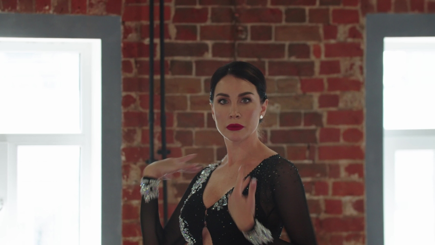 A woman dancer with red lipstick wearing shiny dress dancing in the studio with brick walls