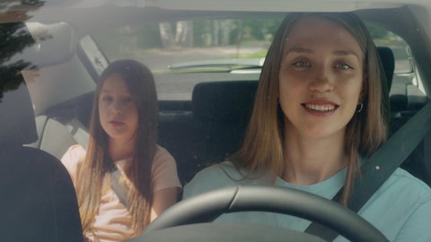 Young family of mother driver and girl in car driving to adventure at morning. Kid looking outside and pretty woman riding by steering wheel. Child and cheerful parent spending time together closeup