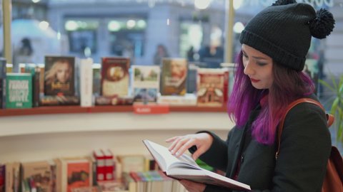 Portrait of stunning asian woman with bright red lips and purple hair reading a book in a bookstore. Millenials lifestyle. teenage student shopping. Concept of hipster style and trends.