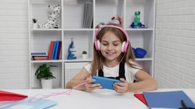happy schoolgirl in headphones watching music video on cell phone in classroom, study online