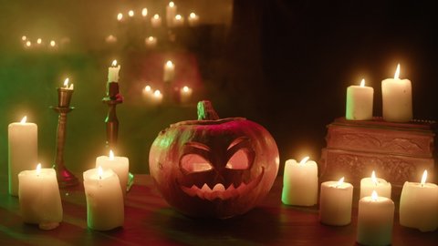 Jack-o-lantern and blowing burning candles close-up. Carved pumpkin with fire flame inside standing on wooden table. Halloween symbols, scary face, traditional autumn holiday decorations. 