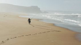 Nazare, Portugal. Drone footage of the a man catching fish with a spinning. Astonishing sandy beach with high tide and cliffs. High quality 4k footage