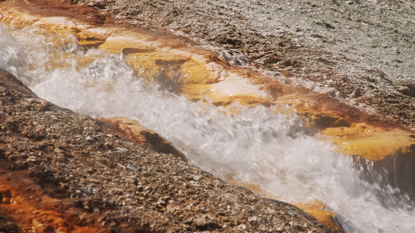 World famous Yellowstone National Park 4K. Slow motion hot water stream flowing down from volcanic geyser basin by iron and cooper mineral elements reach surface. Vibrant orange color hot springs