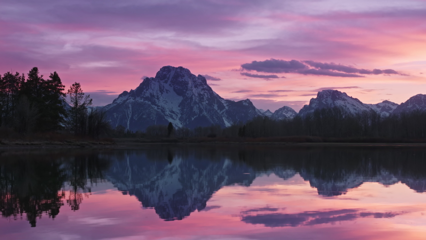 Romantic colorful sunset above clear calm mountain lake. Purple and pink vivid clouds in sky. Majestic winter landscape 4K. Exploring beauty world, travel nature, holidays shot. 4K footage Grand Teton Royalty-Free Stock Footage #1079611076