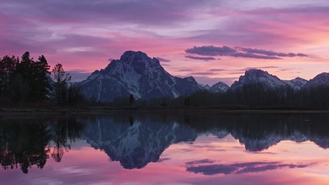 Romantic colorful sunset above clear calm mountain lake. Purple and pink vivid clouds in sky. Majestic winter landscape 4K. Exploring beauty world, travel nature, holidays shot. 4K footage Grand Teton 스톡 비디오