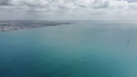 Aerial view of yachts sailing in open Atlantic ocean at coast of Cascais city, Portugal, Europe. Panoramic shot of coast with city buildings. Natural background with blue sea, 4k footage 