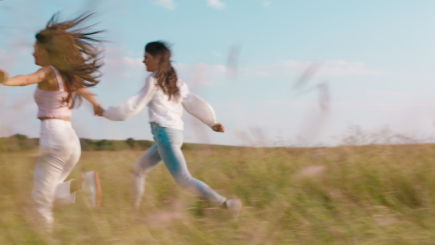 Good looking two young women happy running together through the green field in the middle of nature they speeding good moment together