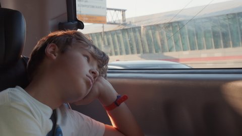Teen boy fastened with seat belt in the car. Child is quite bored and tired with the ride and observing the city with blank look