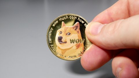 Gold dogecoin coin held between fingers in hand on gey table