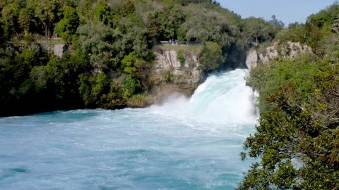 Tiny people in the distance on a viewing platform enjoying watching the giant Huka Falls waterfall on a day out in Taupo, New Zealand Aotearoa