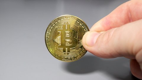 Gold bitcoin coin held between fingers in hand on gey table