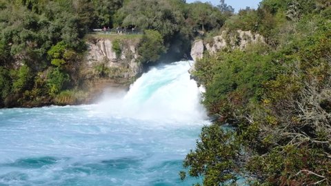 Impressive Huka Falls with people on a viewing platform watching the waterfall on a short walk in Taupo New Zealand Aotearoa. Pan from right to left down river.