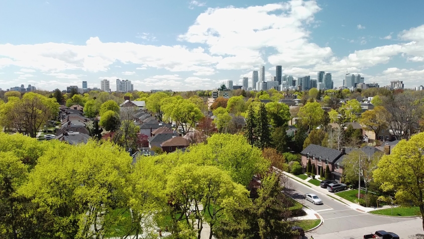 An aerial shot rises from behind a house to reveal a city skyline beyond the trees. | Shutterstock HD Video #1079620298