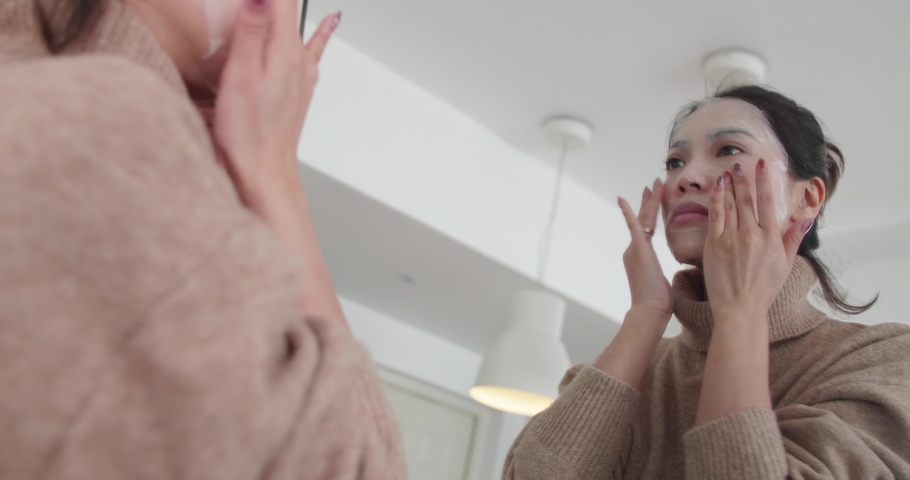 Young Asian woman in front of the mirror applying facial mask at home